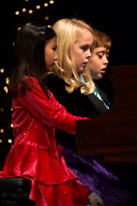 Special events include themed recitals. Three young students perform a piano trio at a recital.
